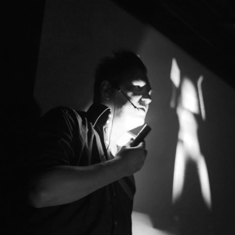 The artist in black and white, lit from a handheld light under his chin.