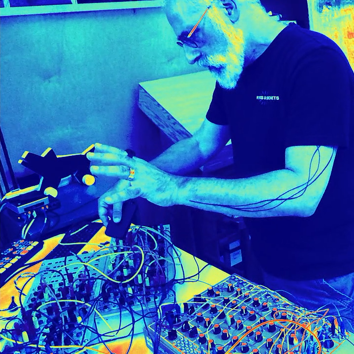 The artist interacts with hardware on a table, a dense configuration of knobs and patch cables.