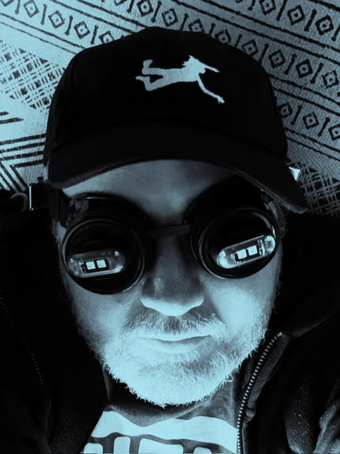 The artist wears dark goggles reflecting mysterious tech.