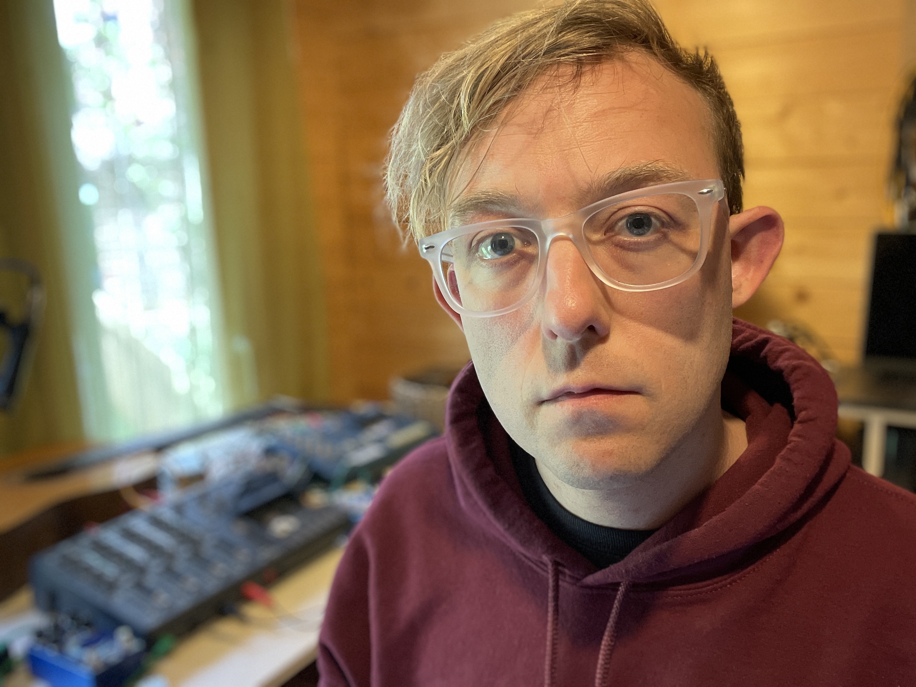 The artist sits in studio. Blurry gear on a wooden desk is visible in the background.